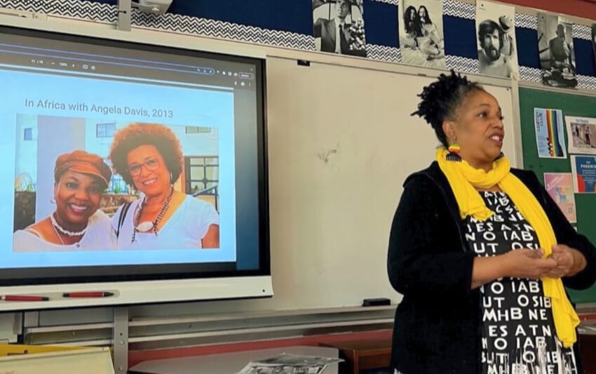 Adult standing in front of a screen projecting an image of herself with the caption In Africa with Angela Davis, 2013