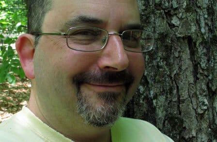 Headshot of poet Neal Levin in front of a tree.