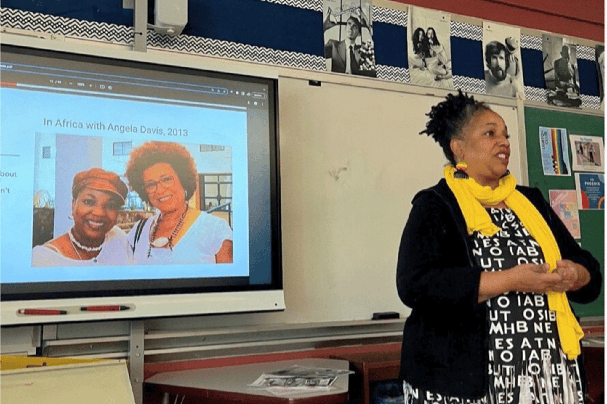 Adult standing in front of a screen projecting an image of herself with the caption In Africa with Angela Davis, 2013