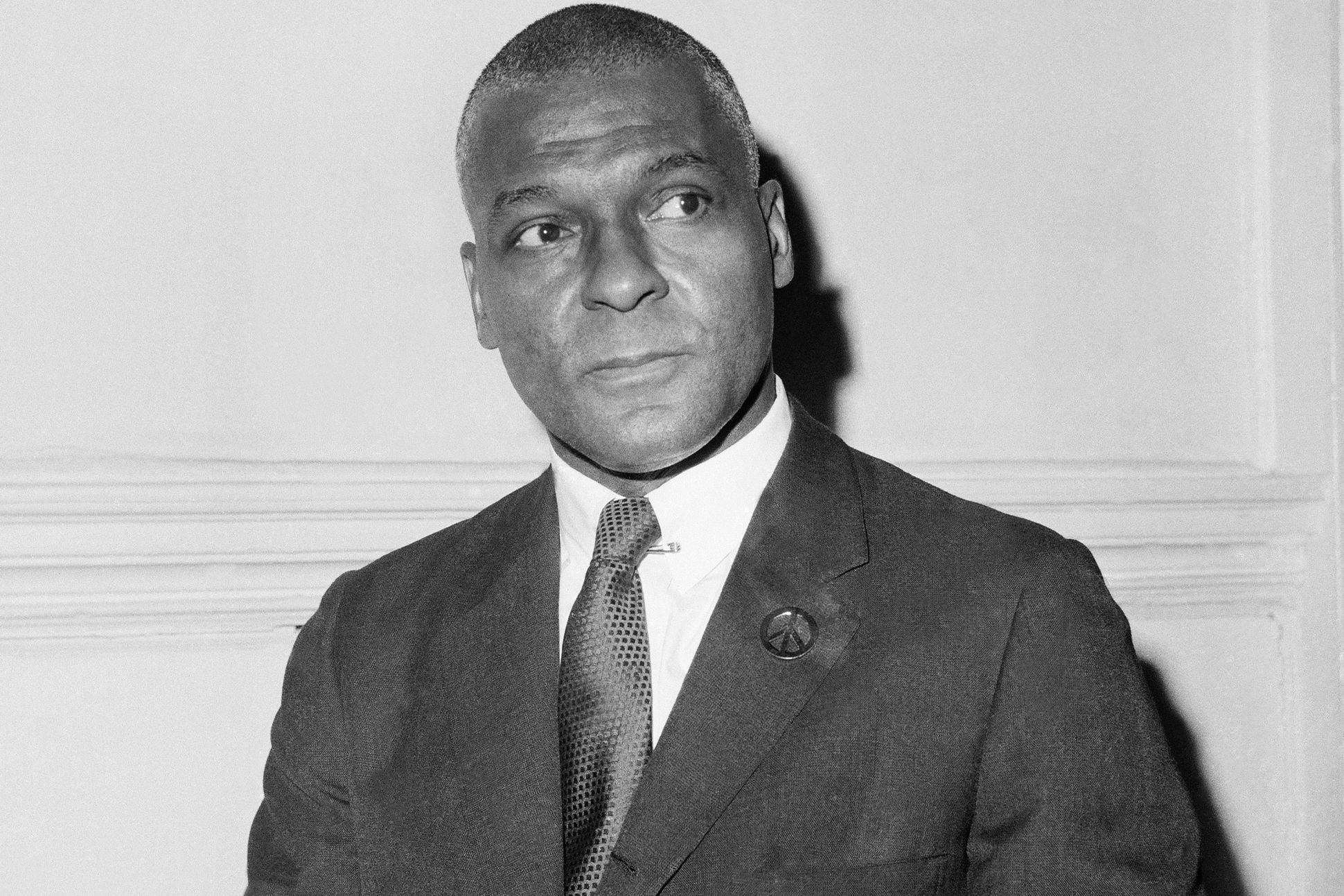 A black-and-white photograph of Bruce M. Wright in a suit and tie, sitting in front of a blank wall.