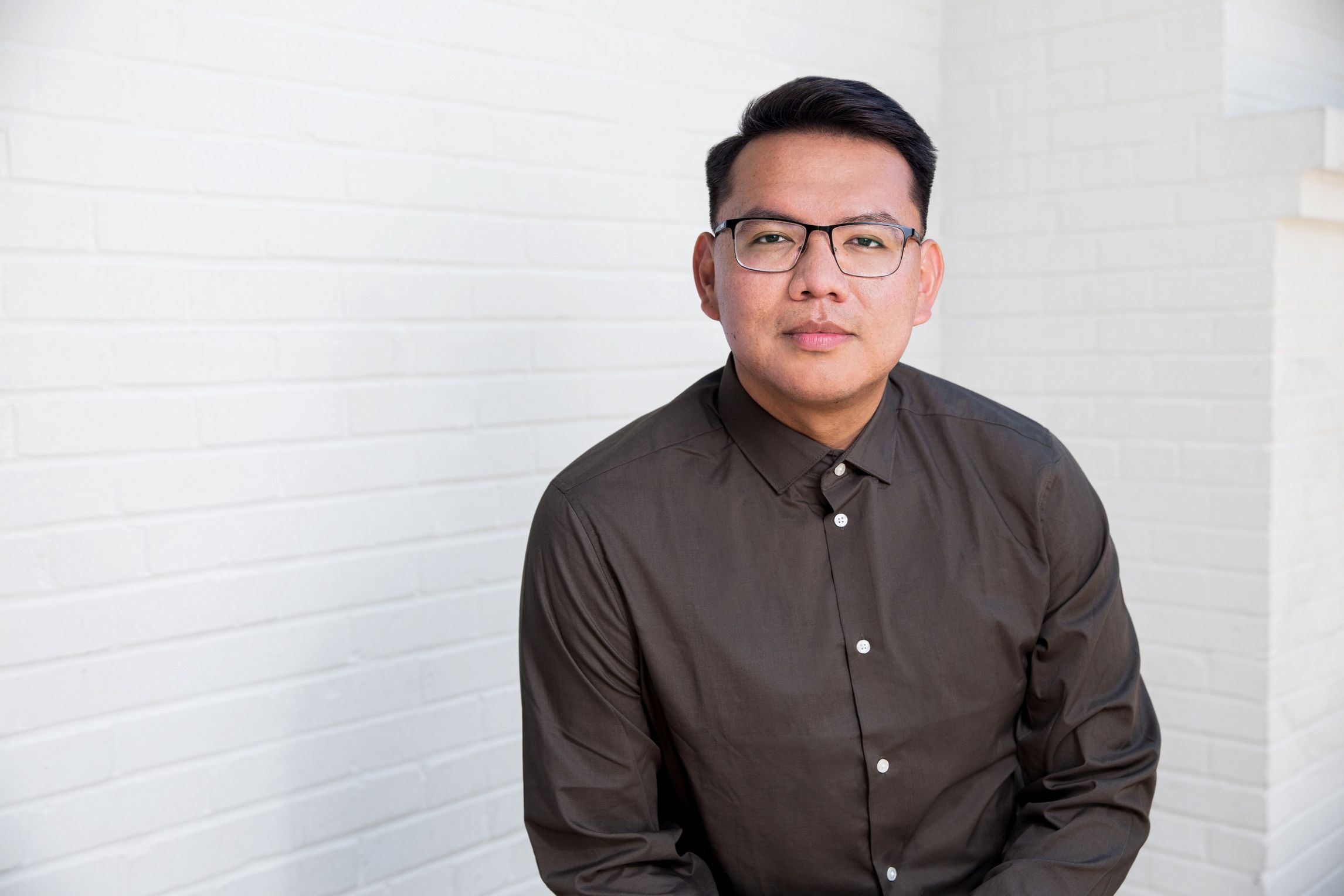 Jake Skeets, with dark hair, sits in front of a white wall, wearing a blue shirt