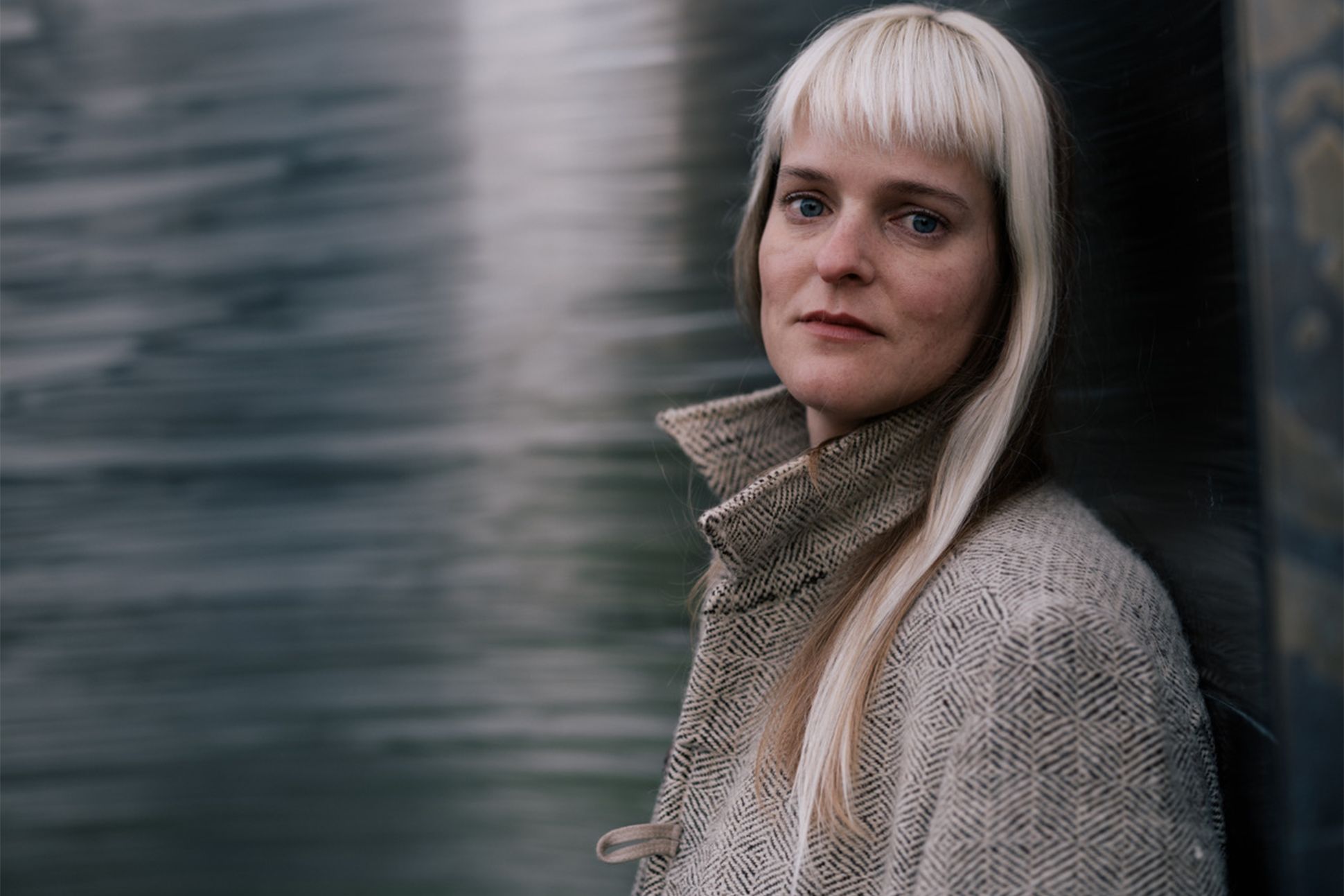 A photograph of Diana Arterian leaning against a wall and looking into the camera.