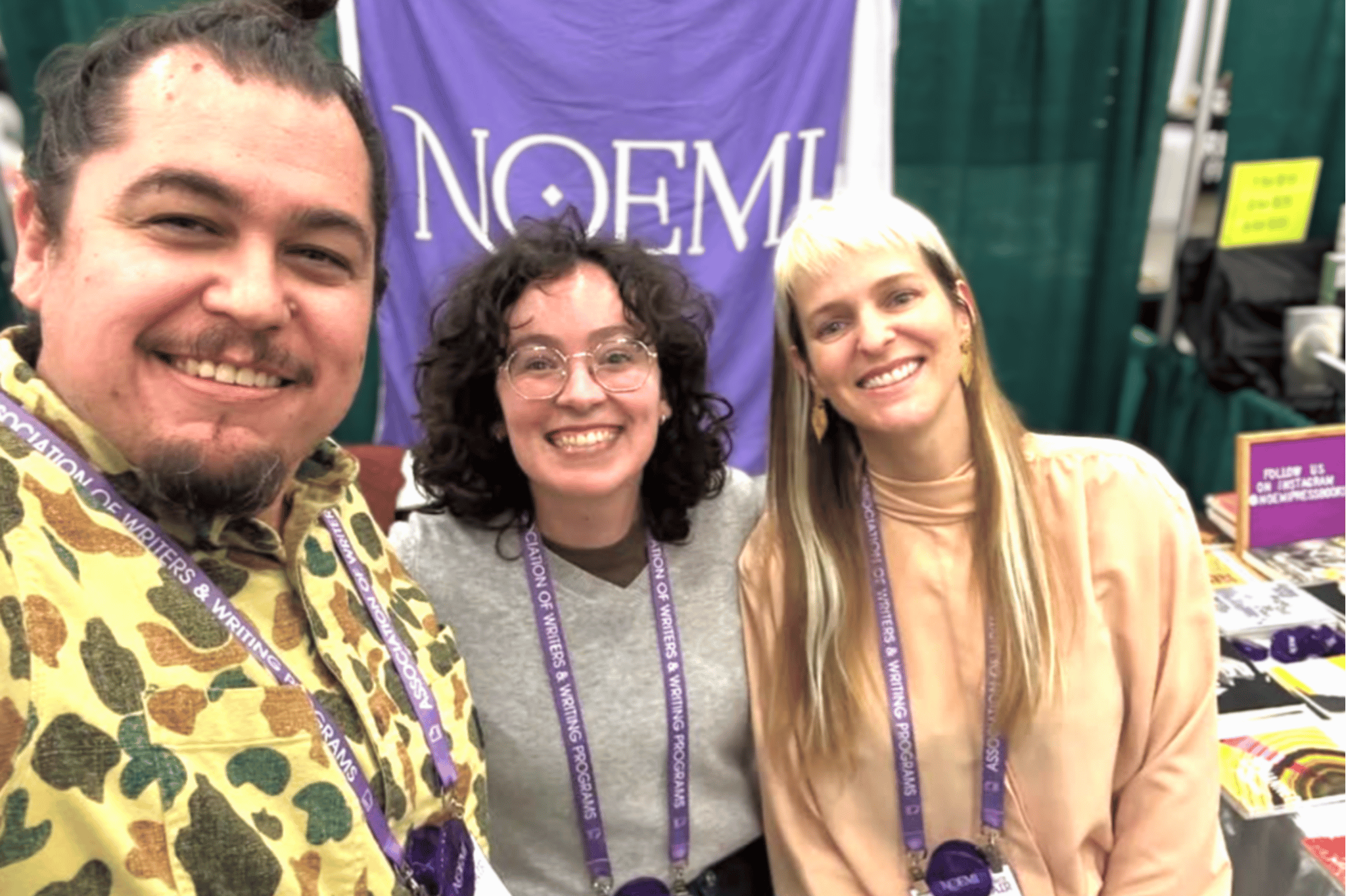 Three adults in front of a purple banner that says NOEMI