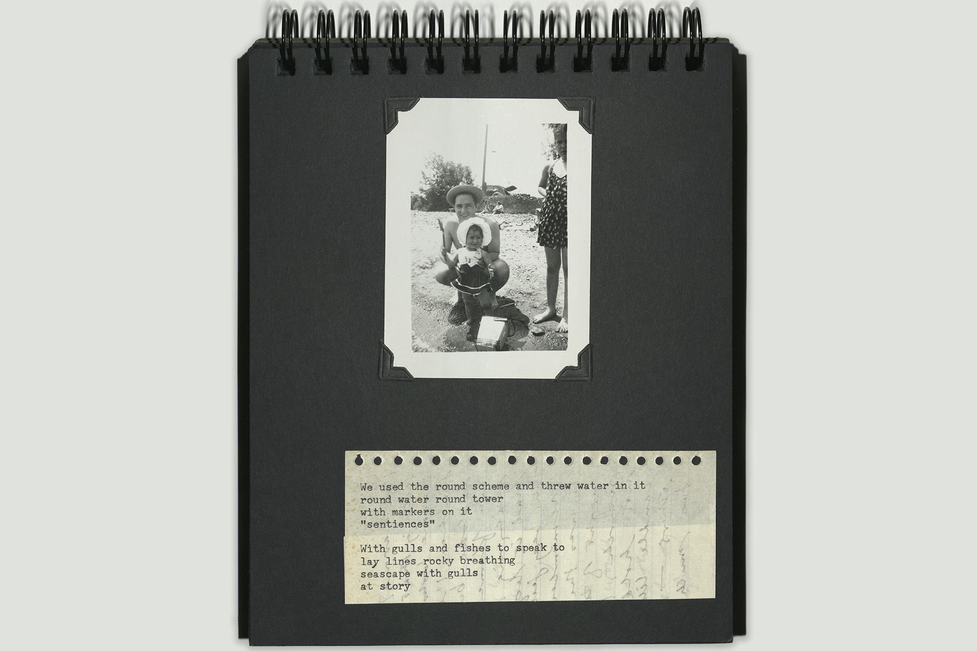 A page from a spiral-bound photo album containing a small, black-and-white photograph of a man holding a child in a bonnet; below is a piece of paper with a typewritten poem.