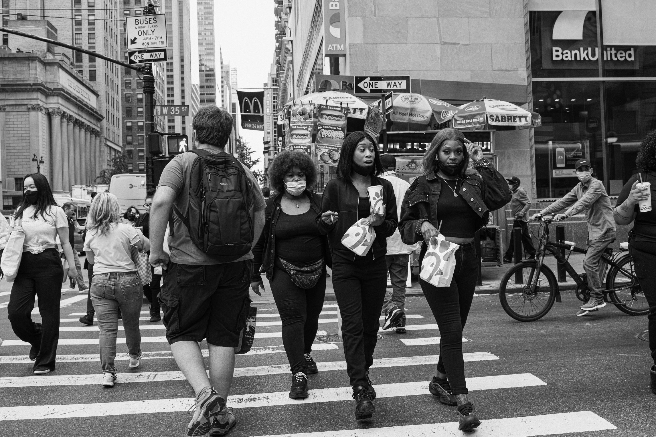 Black and white photograph of three Black women crossing a busy city street holding Chik-fil-A bags and wearing face masks.