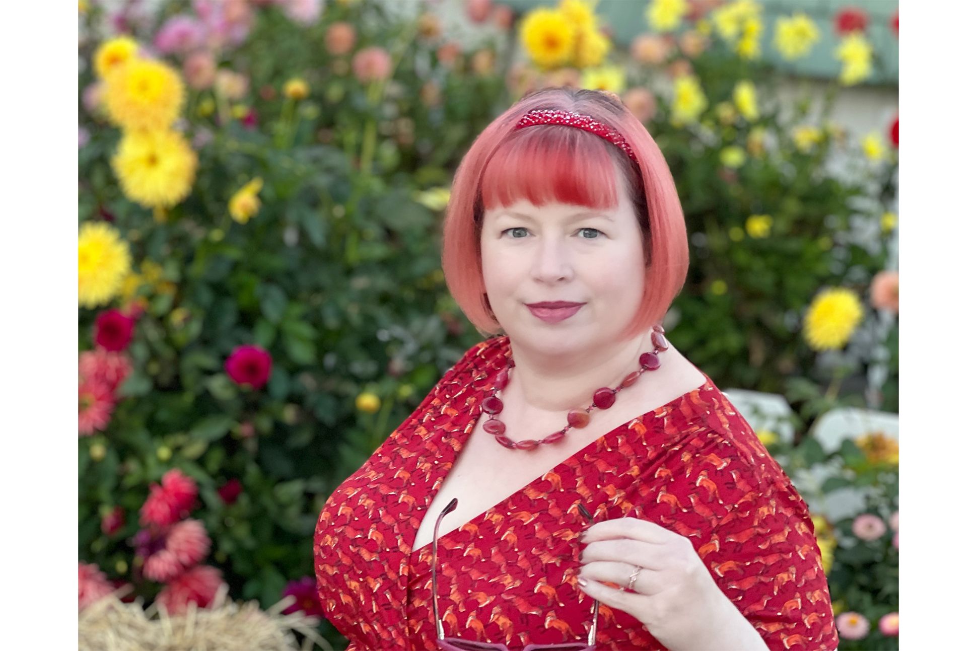 The author wearing a red necklace, red headband, and red dress, in a field of flowers.