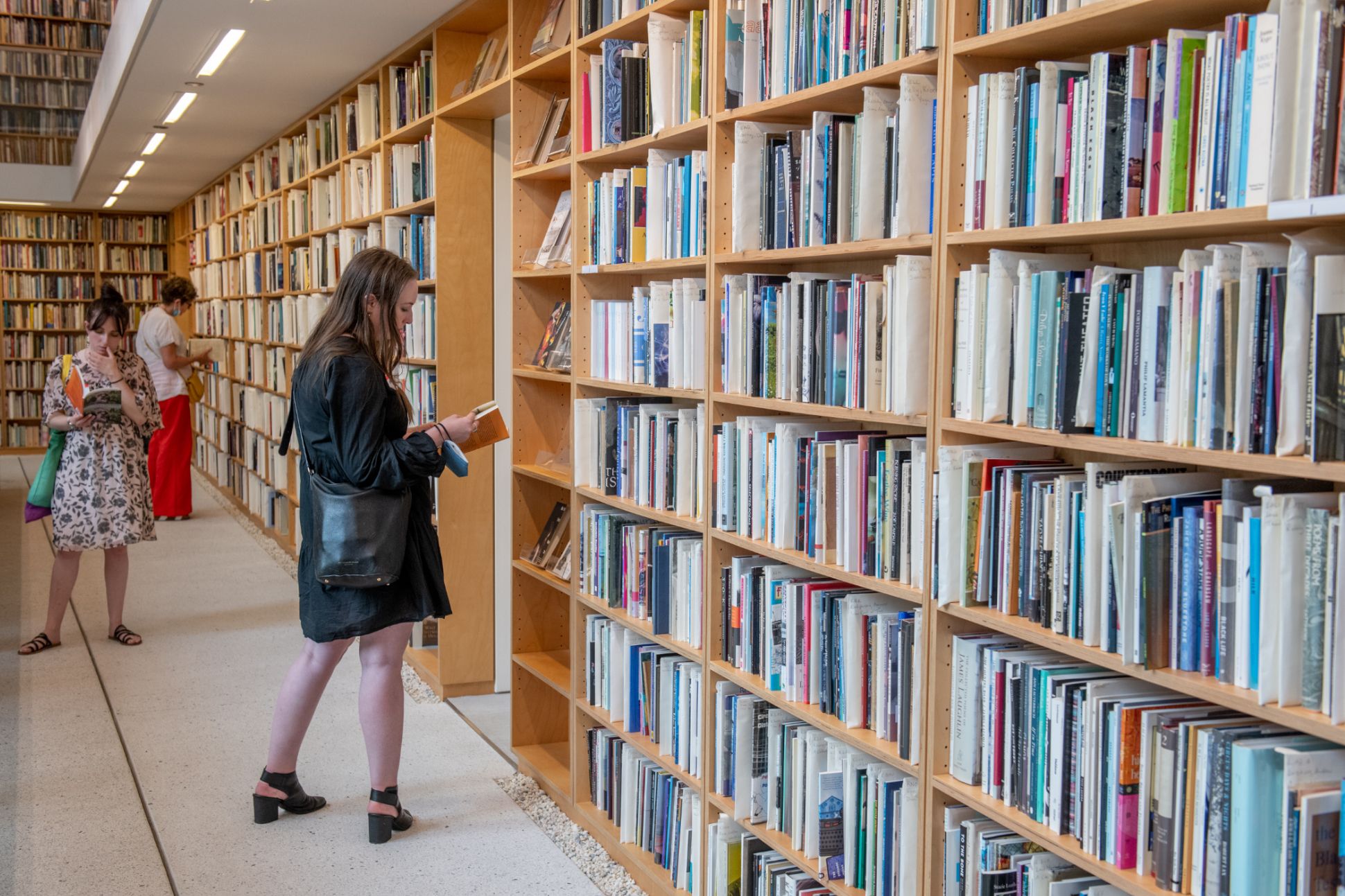 Three people stand in the Poetry Foundation Library, reading books pulled from the shelves.