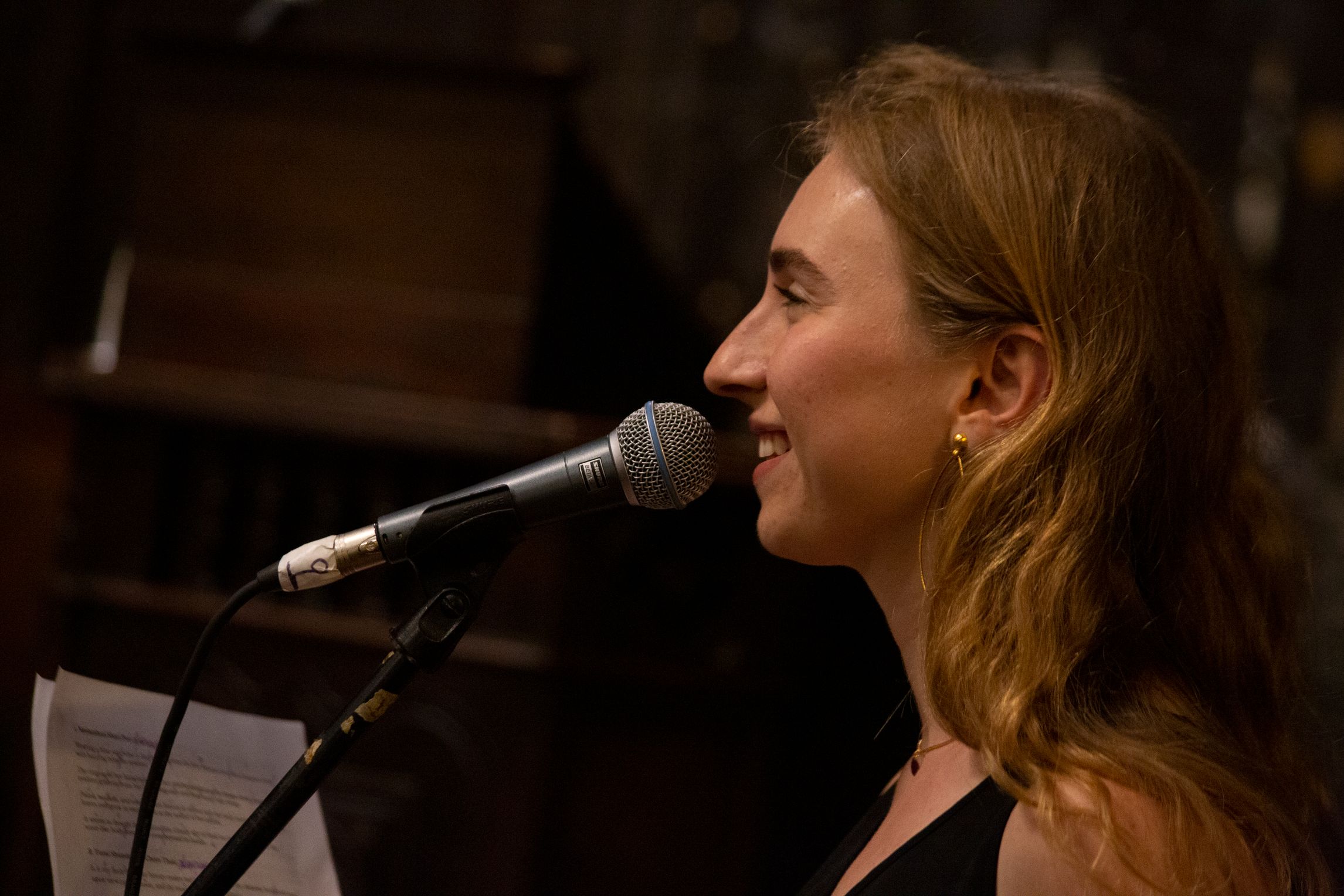 Sasha Burshteyn a white woman is smiling and reading with a microphone her poem.