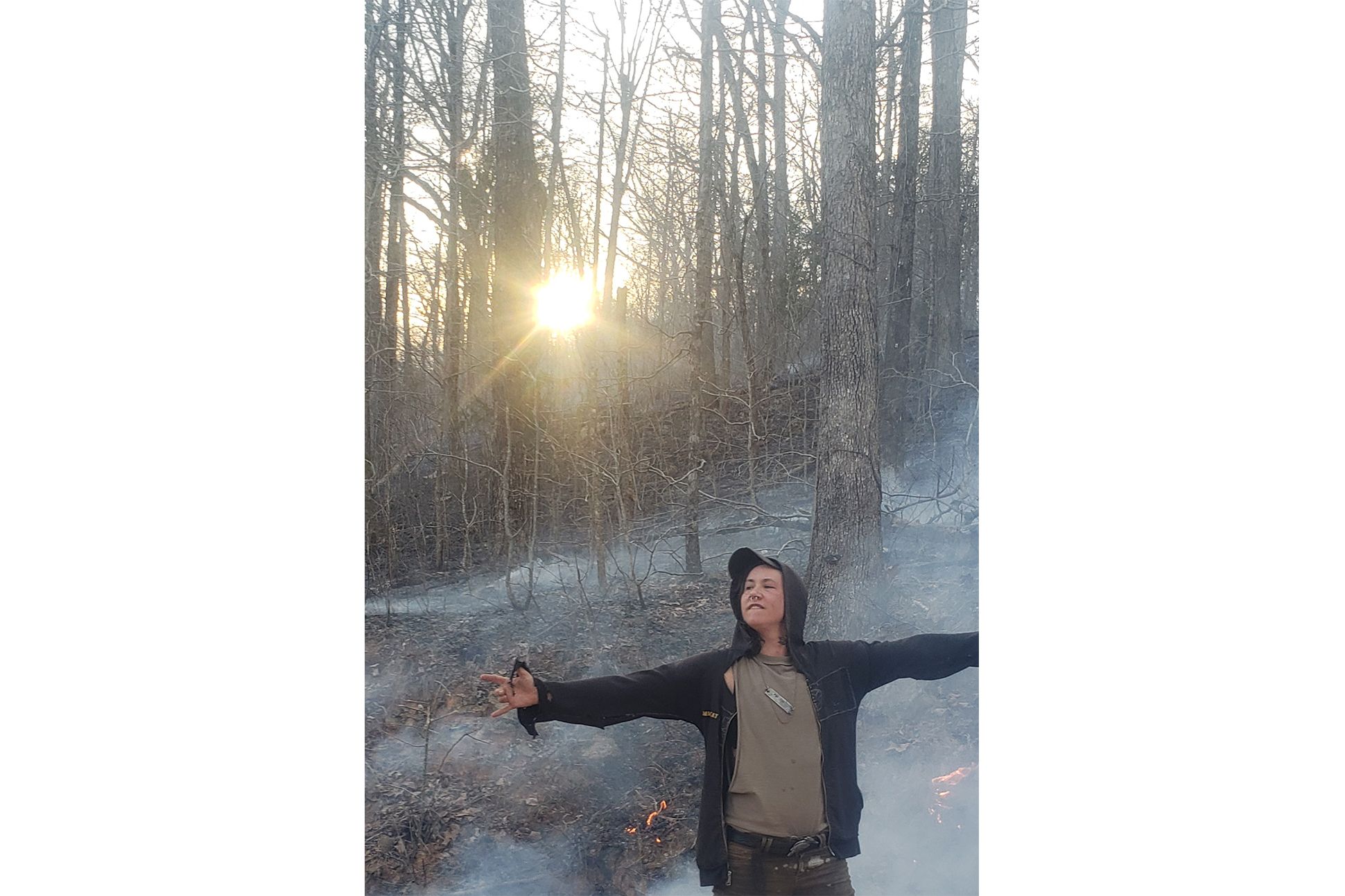 Man in hoodie opening his arms in a forest