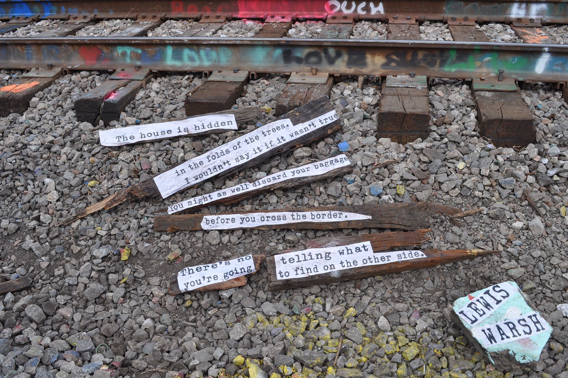 Text from Lewis Warsh's poem "Donatello" is printed on pieces of wood beside railroad tracks
