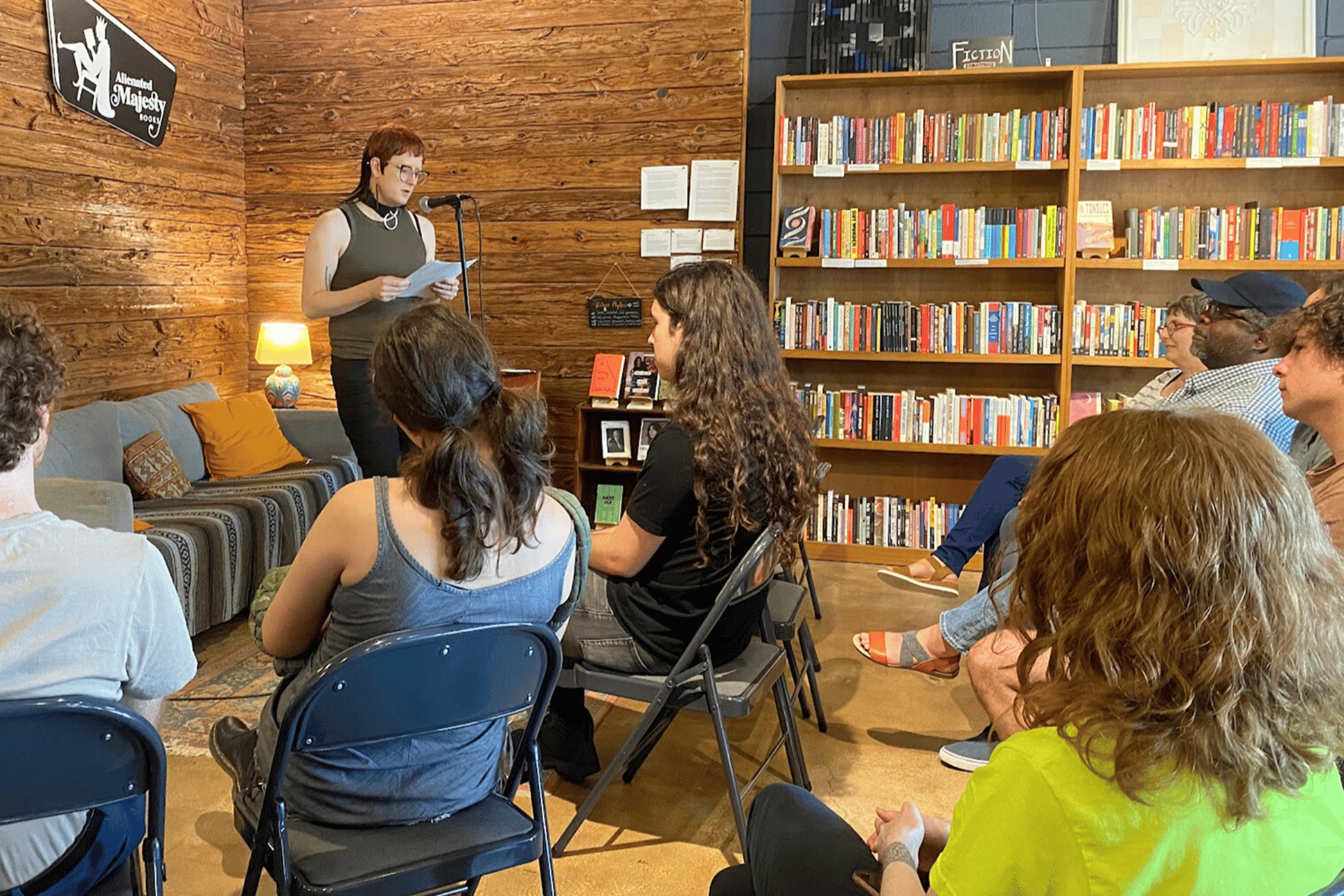 An adult, Amber Isaac, reading a poem at a bookstore with several adults watching.