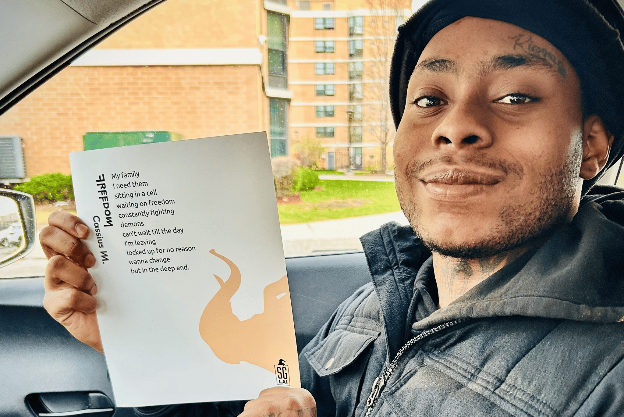 Young man in a car smiling while holding up a poem with the title Freedom