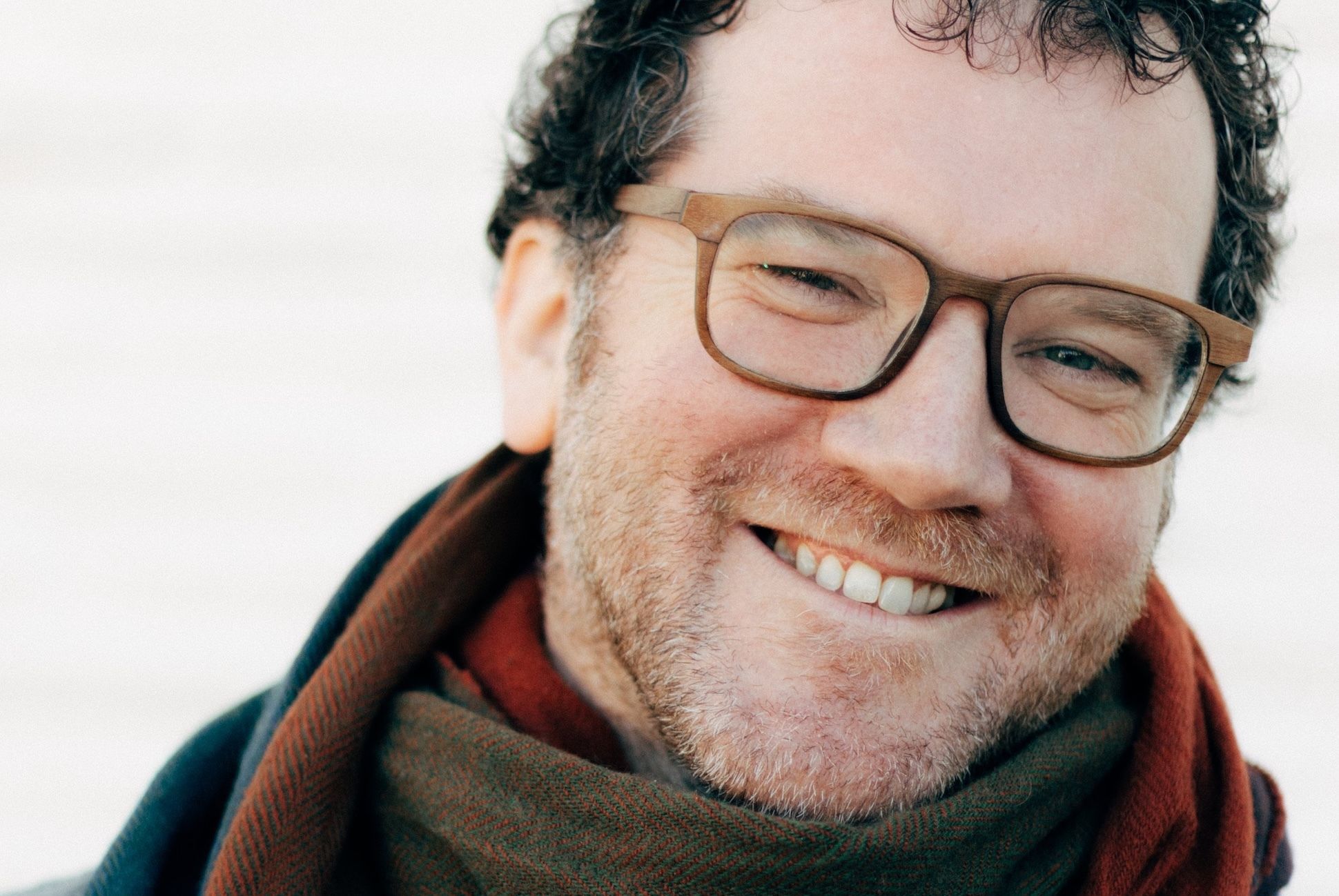 Photo of poet Pádraig Ó Tuama, wearing a grey shirt and a multicoloured woolen scarf.