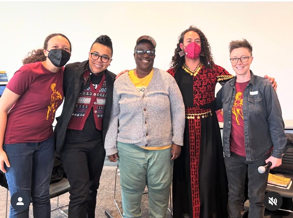 Five adults smiling with their arms linked in front of a white wall