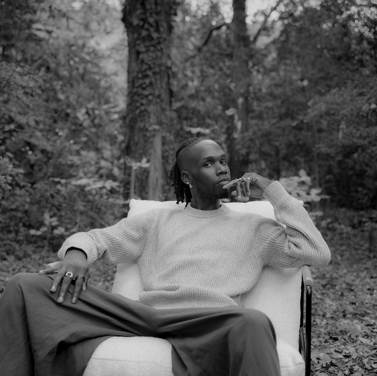 W.J. Lofton, a man with locs in a sweater, sits in a cushioned chair in his backyard.