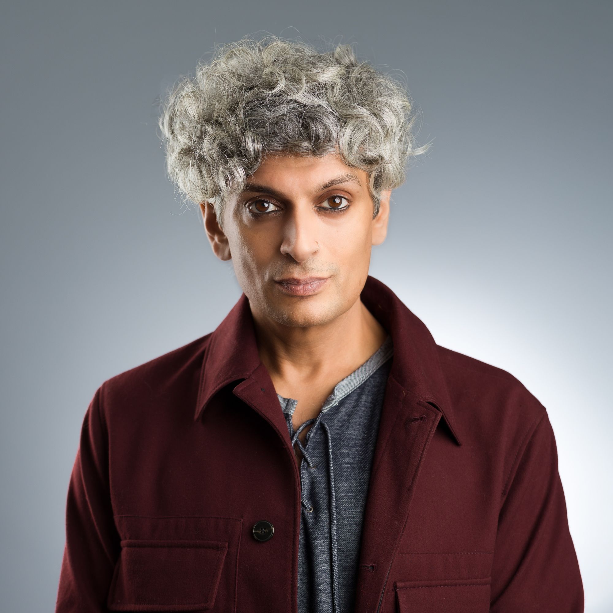 Kazim Ali, a brown man with salt-and-pepper curly hair and smoky eyes, smiles at you.