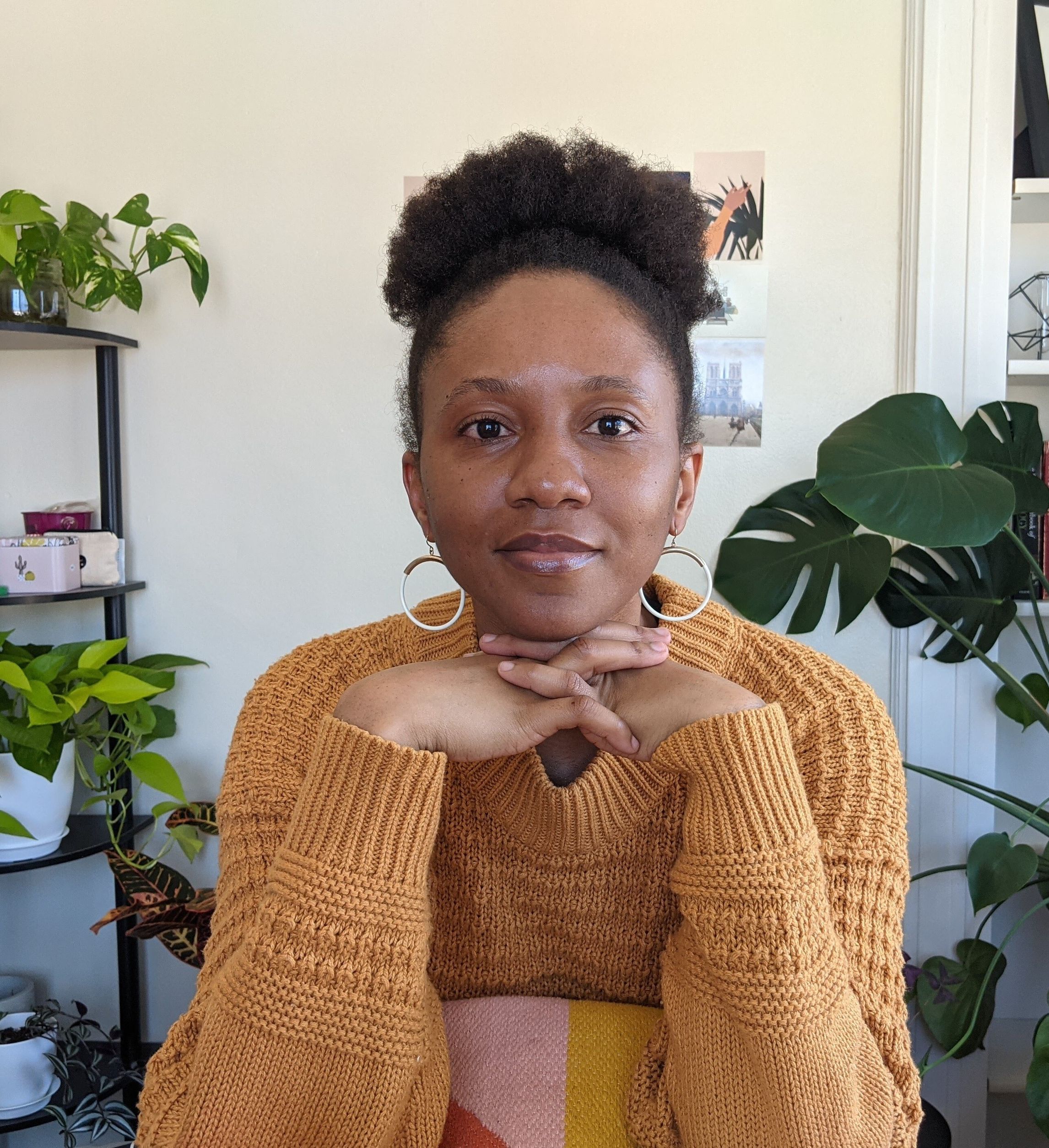 Uche Okonkwo, a black woman with brown haif, sits in front of a wall.
