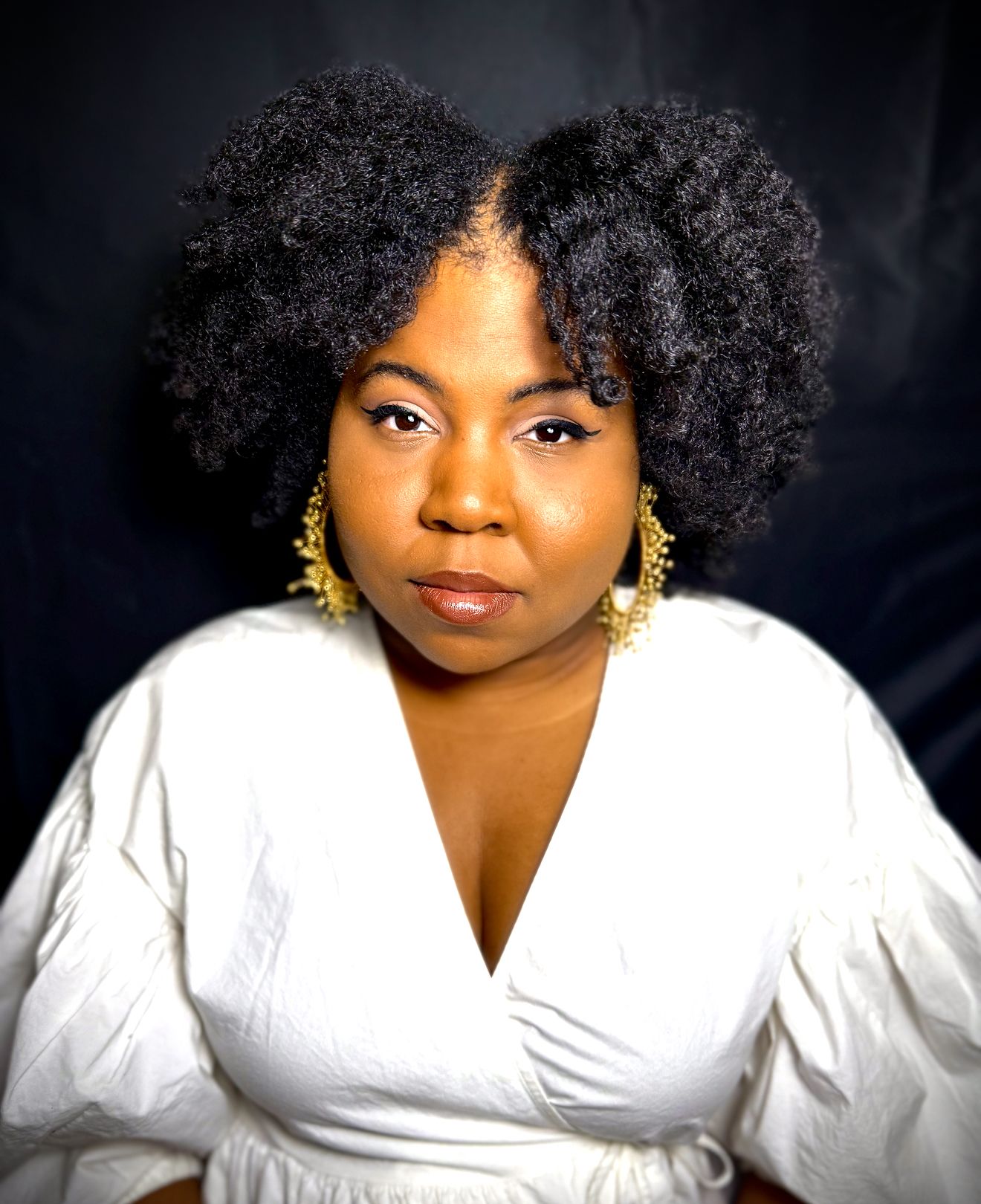 Ashley Jones, a Black woman with black hair and a white shirt sits in front of a black magic