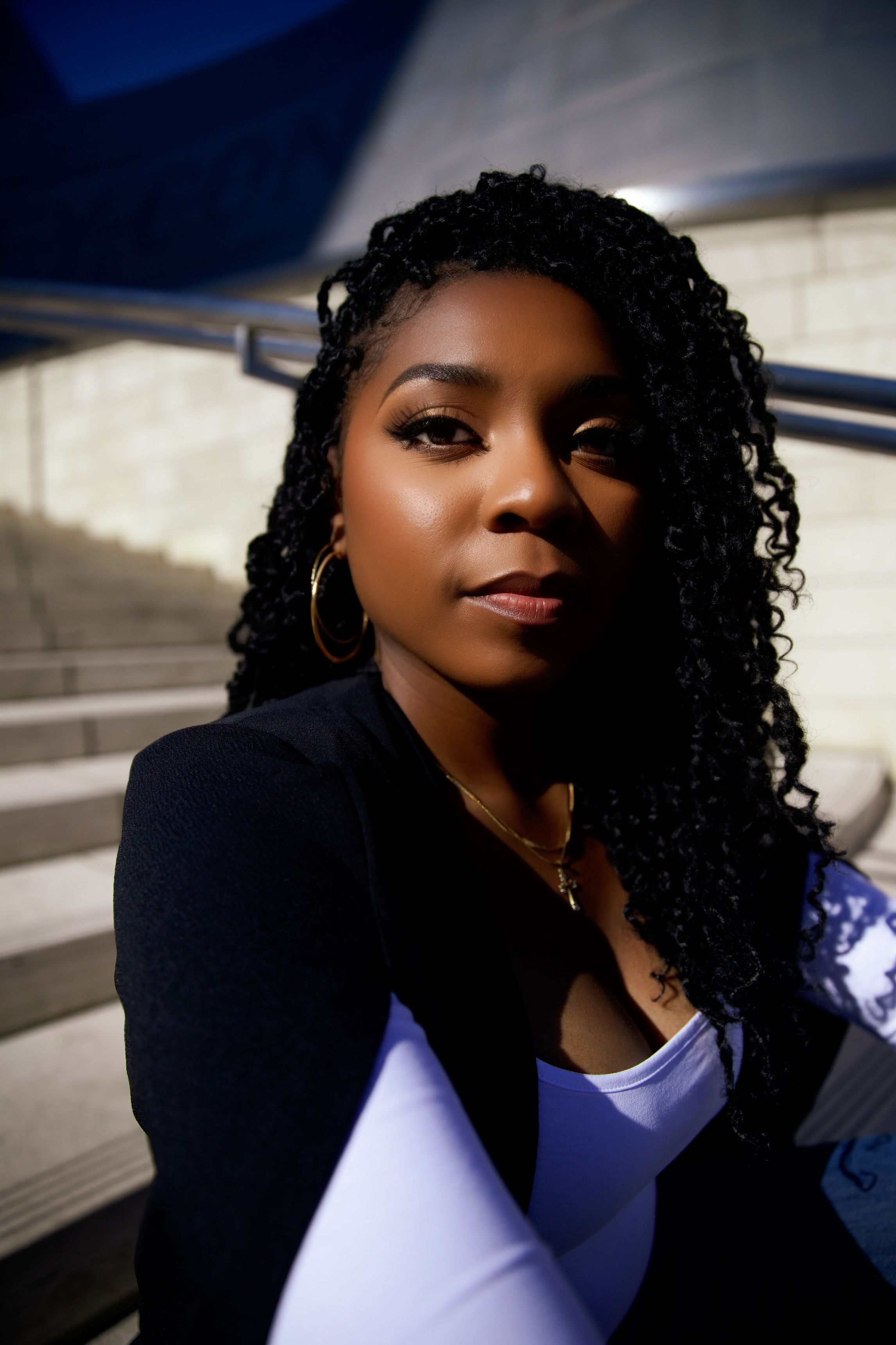 a black woman with black hair in braids sitting on a stoop with a white shirt and black blazer on