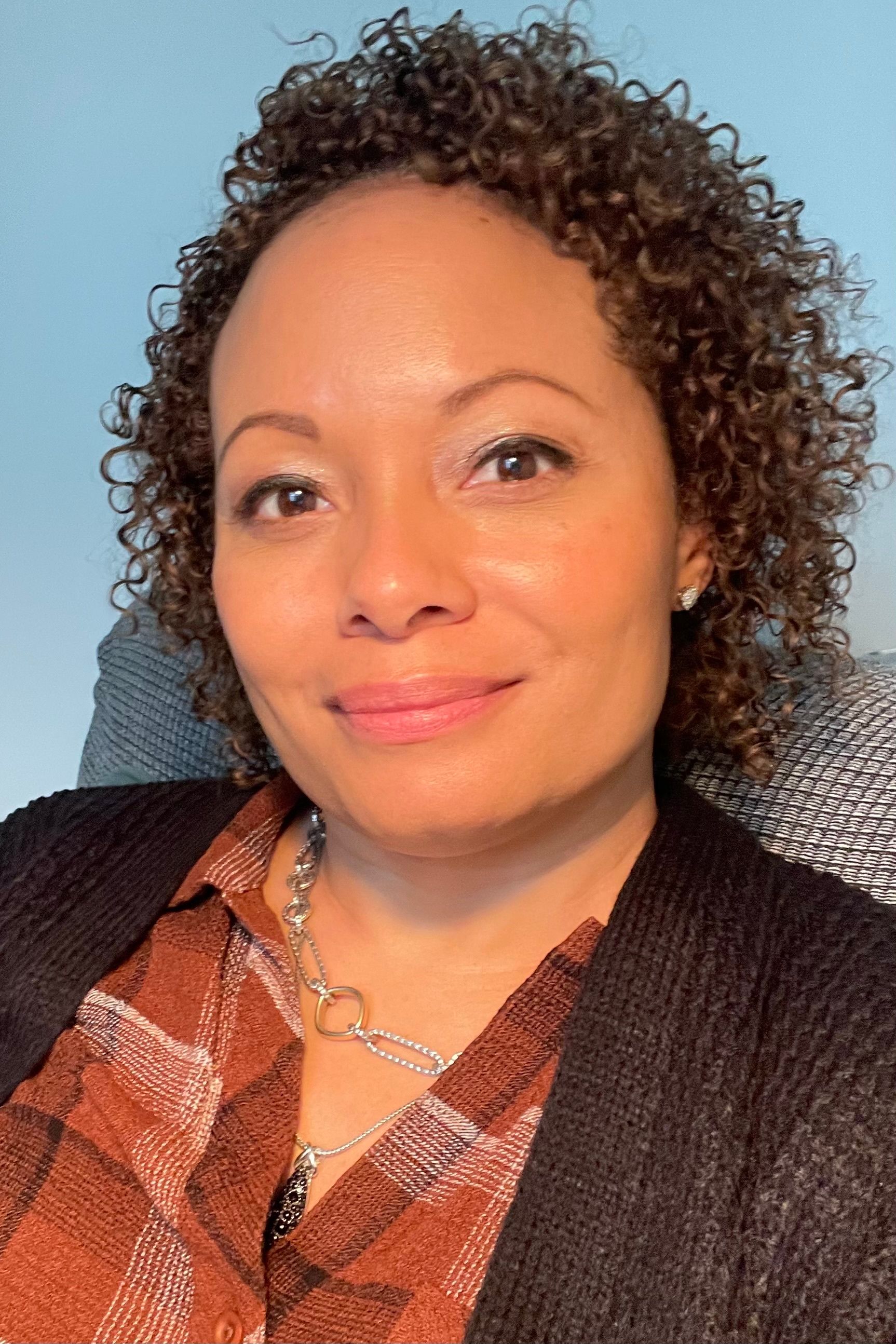 CM Burroughs, a black woman with brown curly hair sits in front of a blue wall.