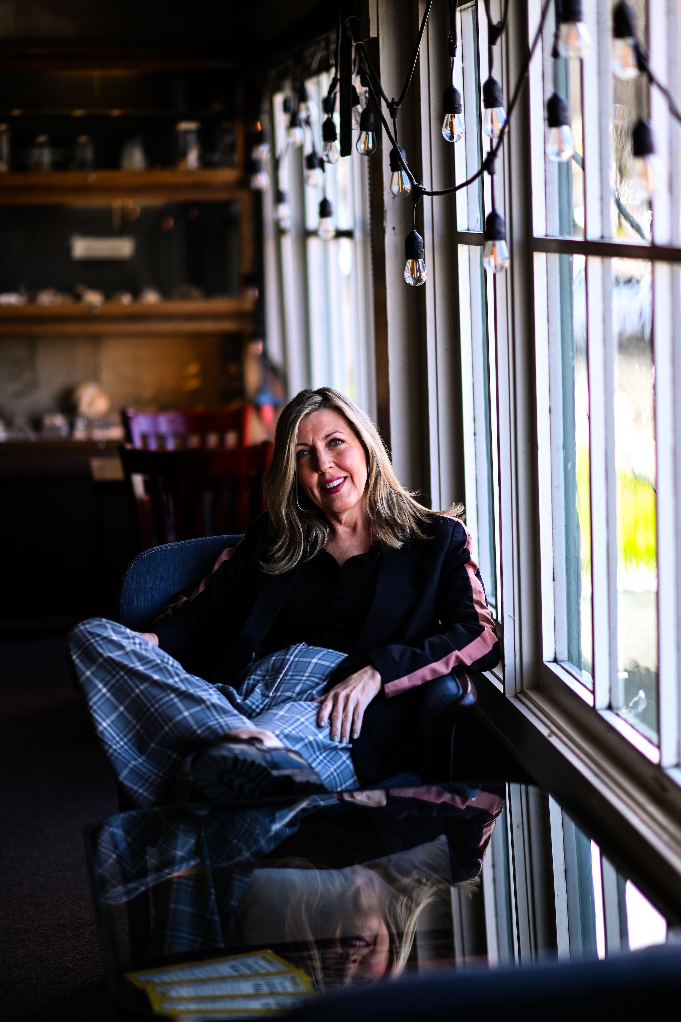 Kelli Russell Agodon, a white female in a dark top and plaid trousers sitting crosslegged in a restaurant.
