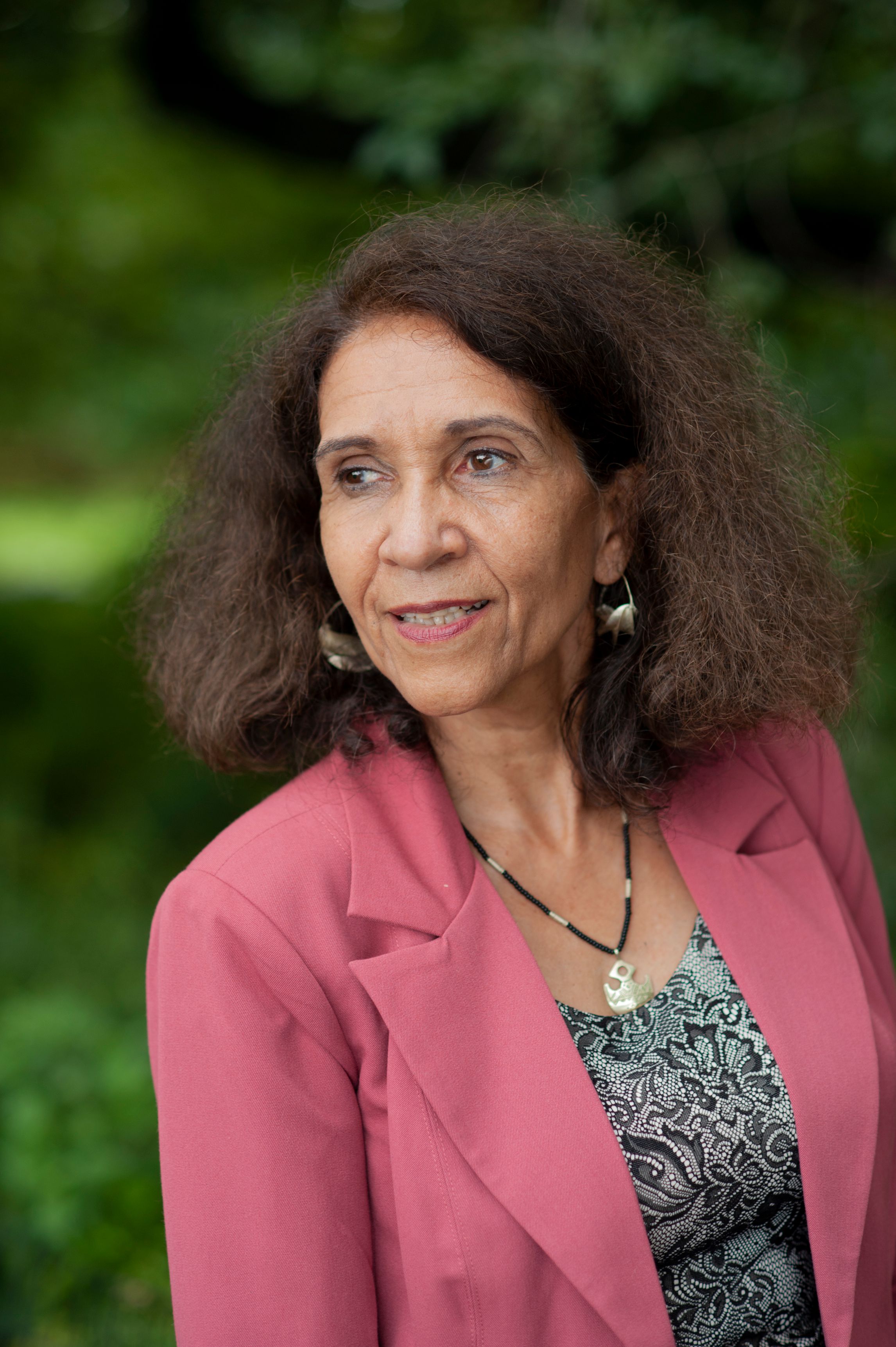 Sylvie Kandé, a woman with curly hair in a pink blazer looking sideway.